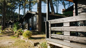 A rustic cabin-style lodging area with wooden structures, a dirt path, and surrounding trees.