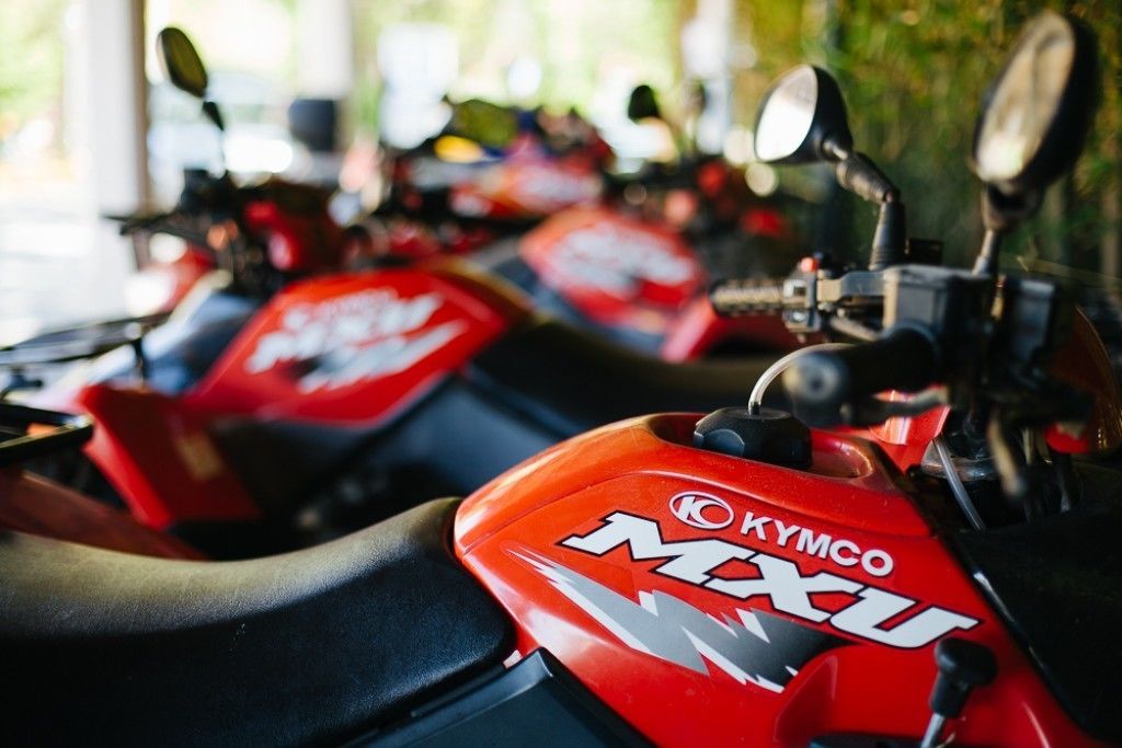 A row of red motorcycles with the brand "KYMCO MXU" visible on the fuel tanks.