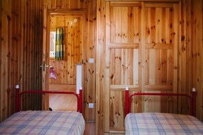 A wooden room with two beds, a door, and a window with a curtain.