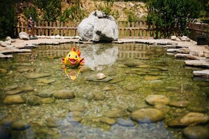 A clear pond with a toy fish in the center, surrounded by rocks and a wooden fence. - Camping Rural Ría de Arosa II (Ribeira)