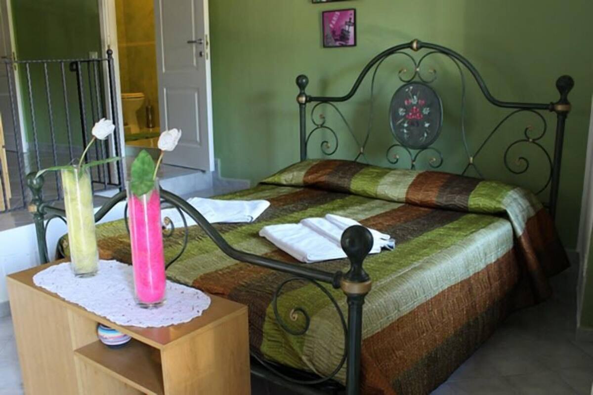 A neatly made bed with a patterned bedspread, a bedside table with a vase of flowers, and a wall clock.