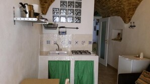 A compact kitchen with a sink, stove, and a small countertop. There is a shelf above the sink holding kitchen utensils. - B&B Santantonio (Crecchio)