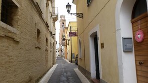 A narrow street with buildings on either side, a clock tower in the distance, and a pink heart decoration on a door. - B&B Santantonio (Crecchio)