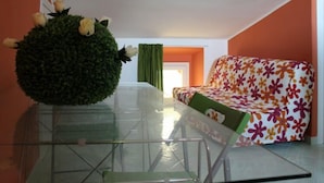 A modern living room with a glass coffee table, a round green plant, and a colorful sofa. - B&B Santantonio (Crecchio)