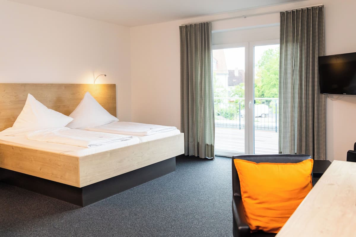A hotel room with a bed, a desk, a chair, a television, and a balcony with curtains.