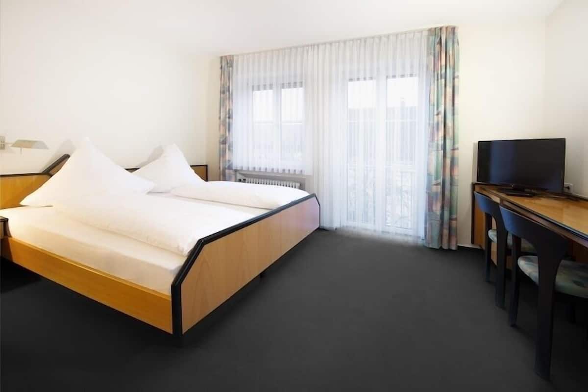 A hotel room with a double bed, a desk with a chair, a television, and a window with curtains.