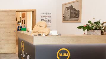 A hotel reception desk with a wooden counter, a welcome sign, and a framed picture on the wall.