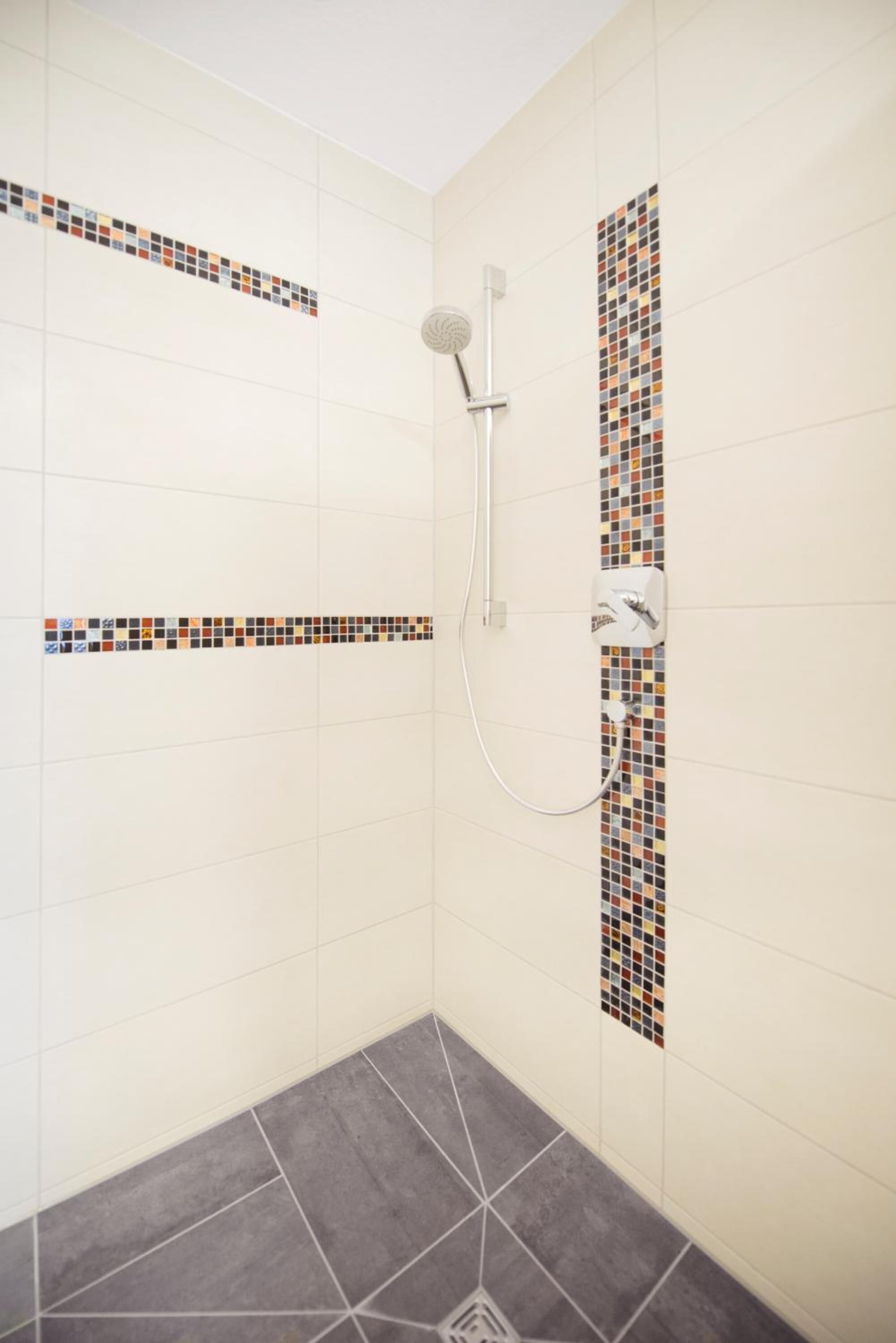 A shower with a tiled wall and a tiled floor.