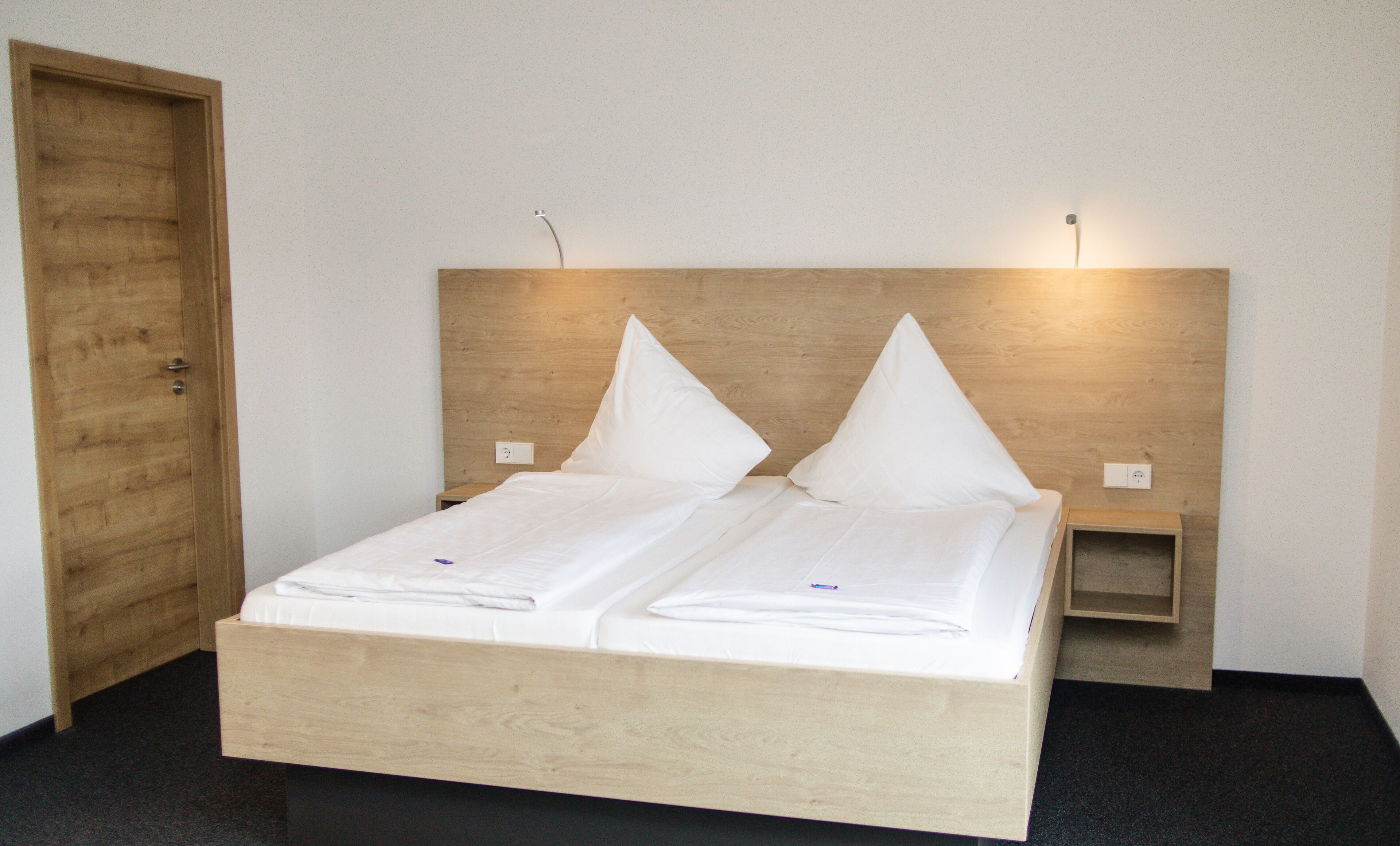 A double bed with a wooden headboard, two bedside tables, and a wooden door.