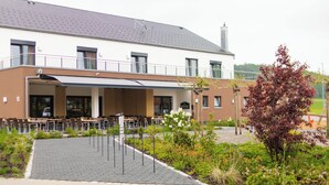 Ein modernes Gebäude mit Flachdach, überdachter Außenbereich und Garten mit verschiedenen Pflanzen und Blumen.