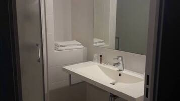 Un baño moderno con lavamanos, espejo y toallero blancos.
