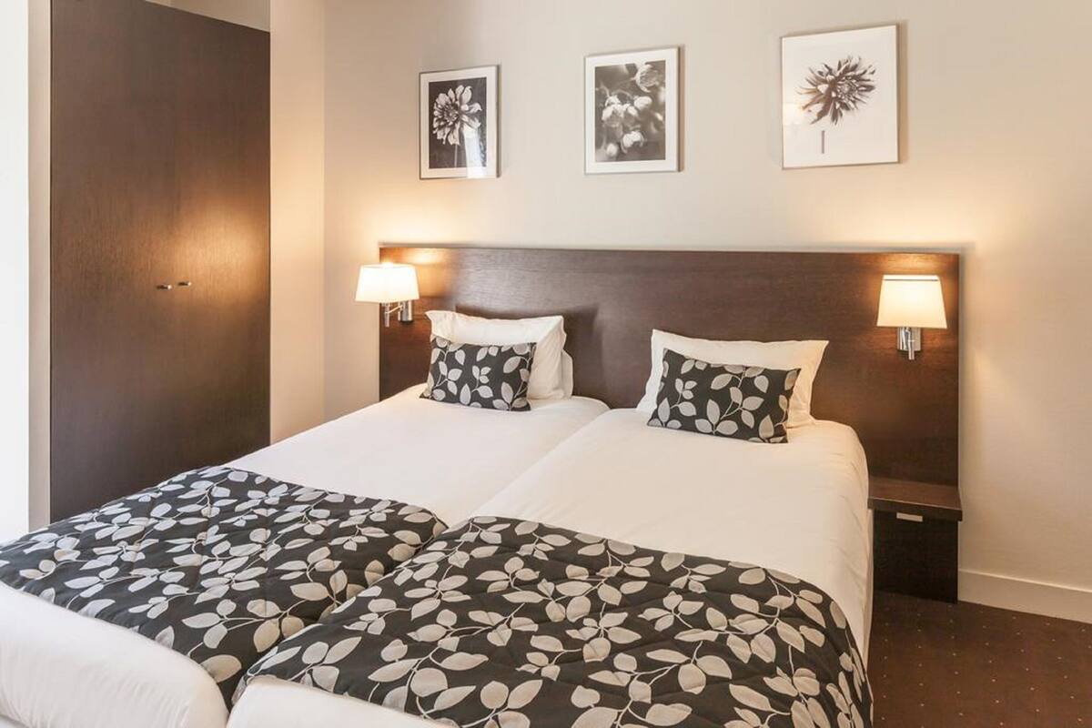 Una cama doble con una colcha estampada con motivos de hojas, dos lámparas de noche y tres cuadros en la pared.