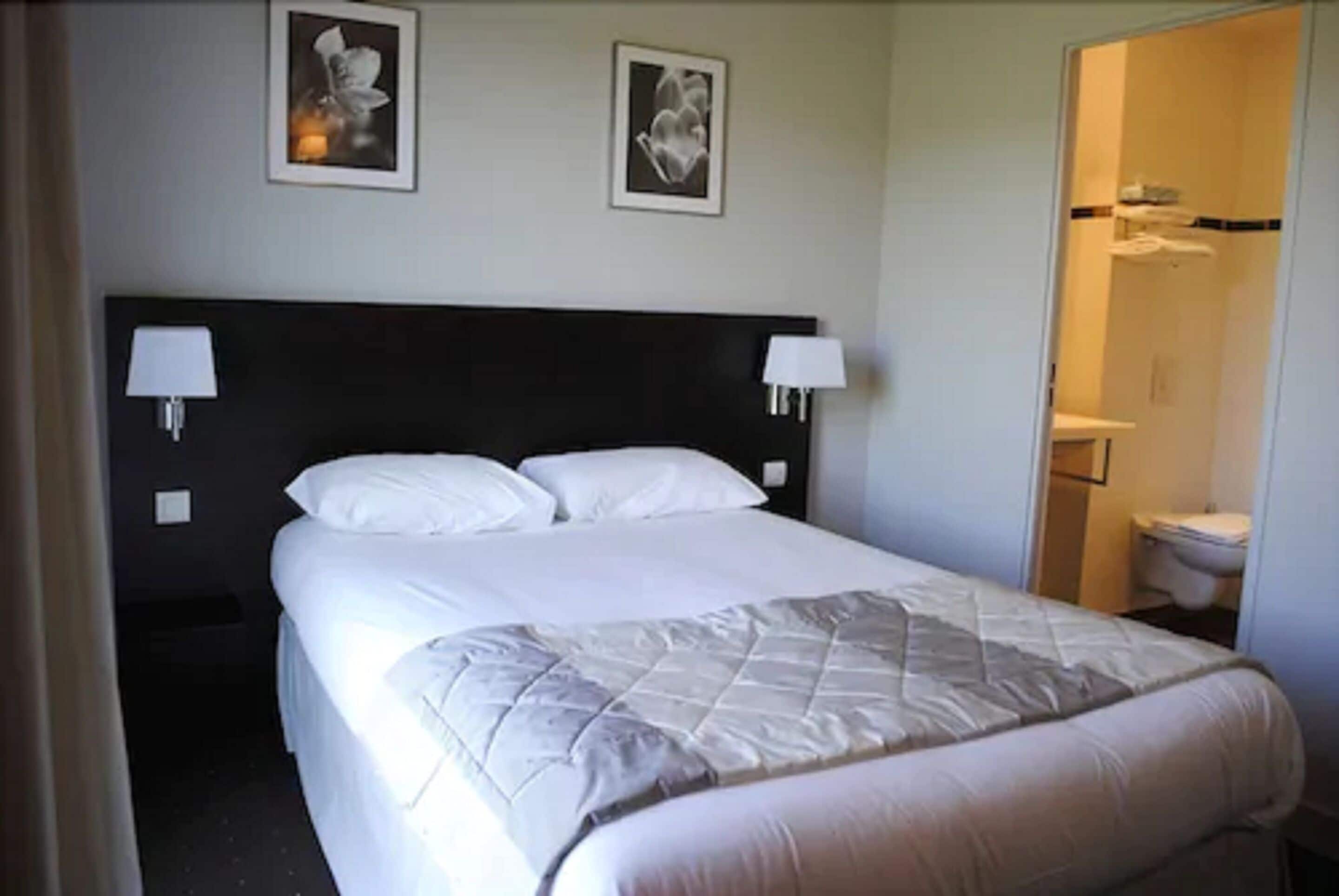 Een hotelkamer met een groot bed, twee wandlampen en een ingelijst kunstwerk boven het bed.