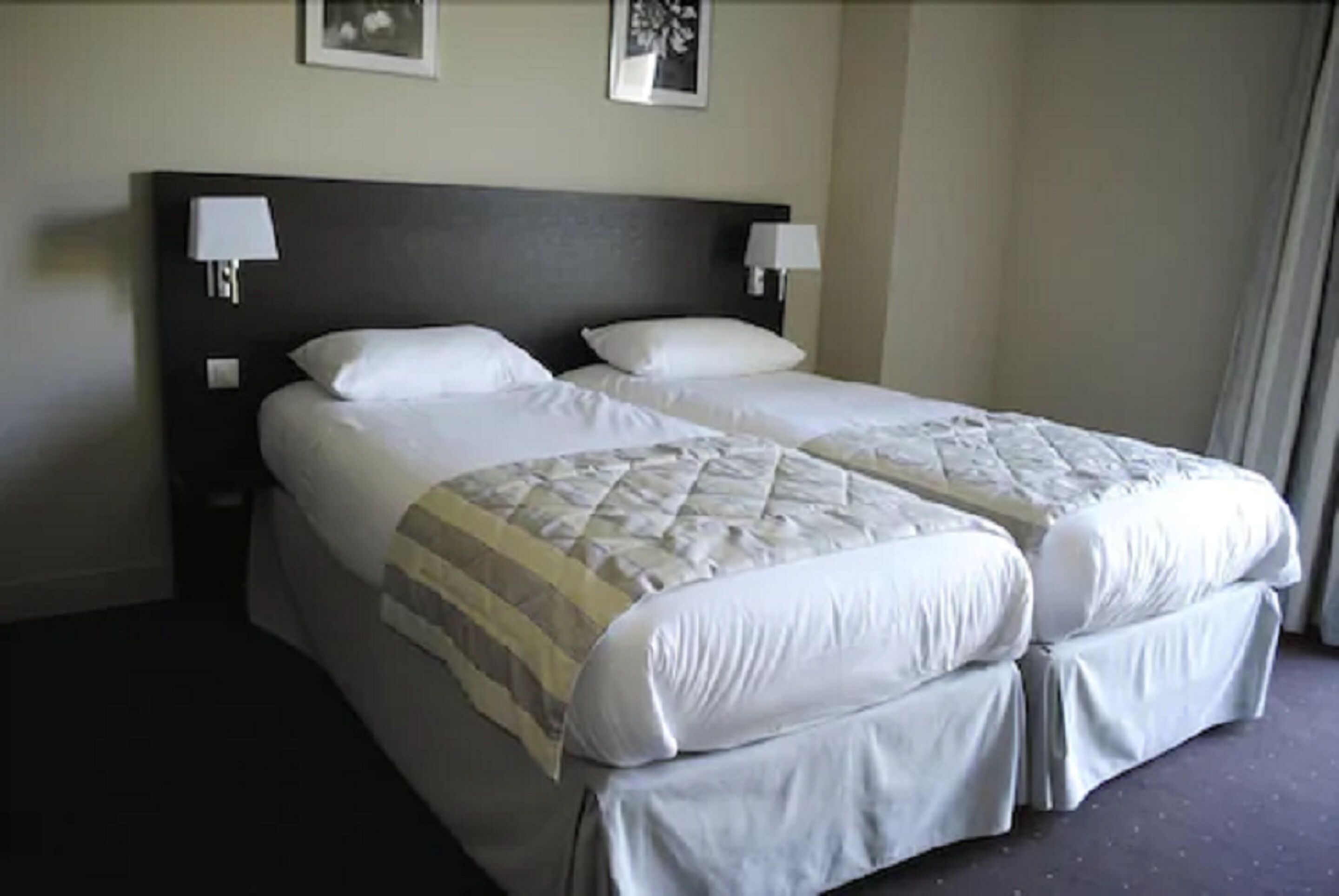 Una cama doble con cubrecama acolchado y dos almohadas, una mesita de noche con lámpara, y un cuadro enmarcado en la pared.
