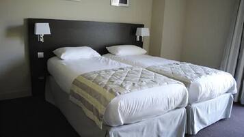 Una cama doble con cubrecama acolchado y dos almohadas, una mesita de noche con lámpara, y un cuadro enmarcado en la pared.