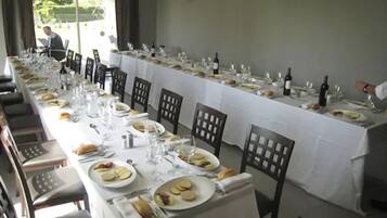 Een lange eettafel gedekt voor een maaltijd, met stoelen, borden, bestek en wijnglazen.