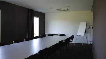 Une salle de conférence avec une longue table, des chaises, un tableau blanc et une fenêtre.
