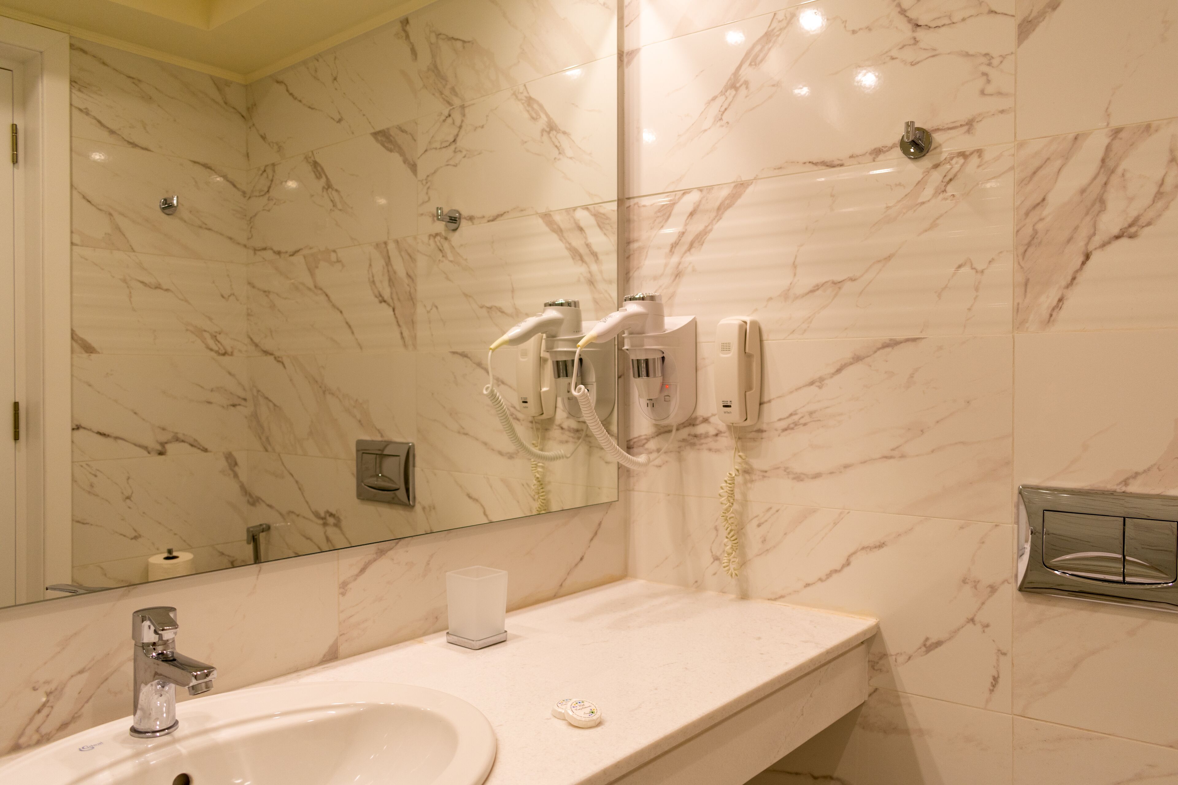 A bathroom with a marble wall, a sink, a mirror, and a hairdryer.