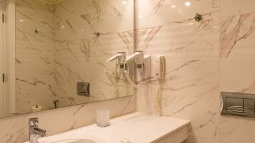 A bathroom with a marble wall, a sink, a mirror, and a hairdryer.