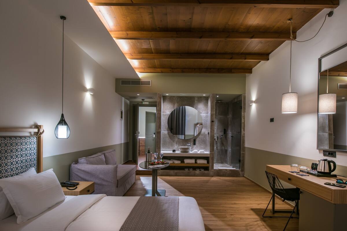 Une chambre d’hôtel moderne avec un plafond en bois, un grand lit, un bureau et une salle de bain équipée d’un miroir et d’un lavabo.