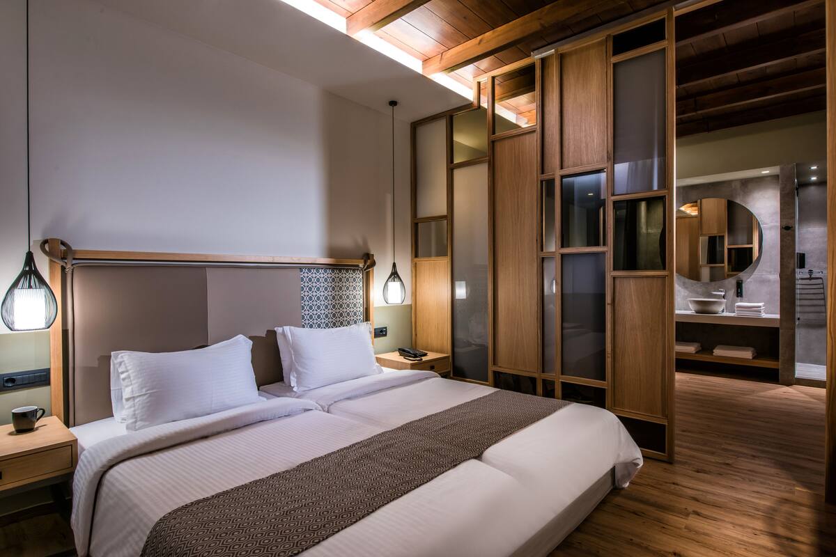 Une chambre d’hôtel moderne avec un grand lit, une tête de lit en bois et une lucarne.