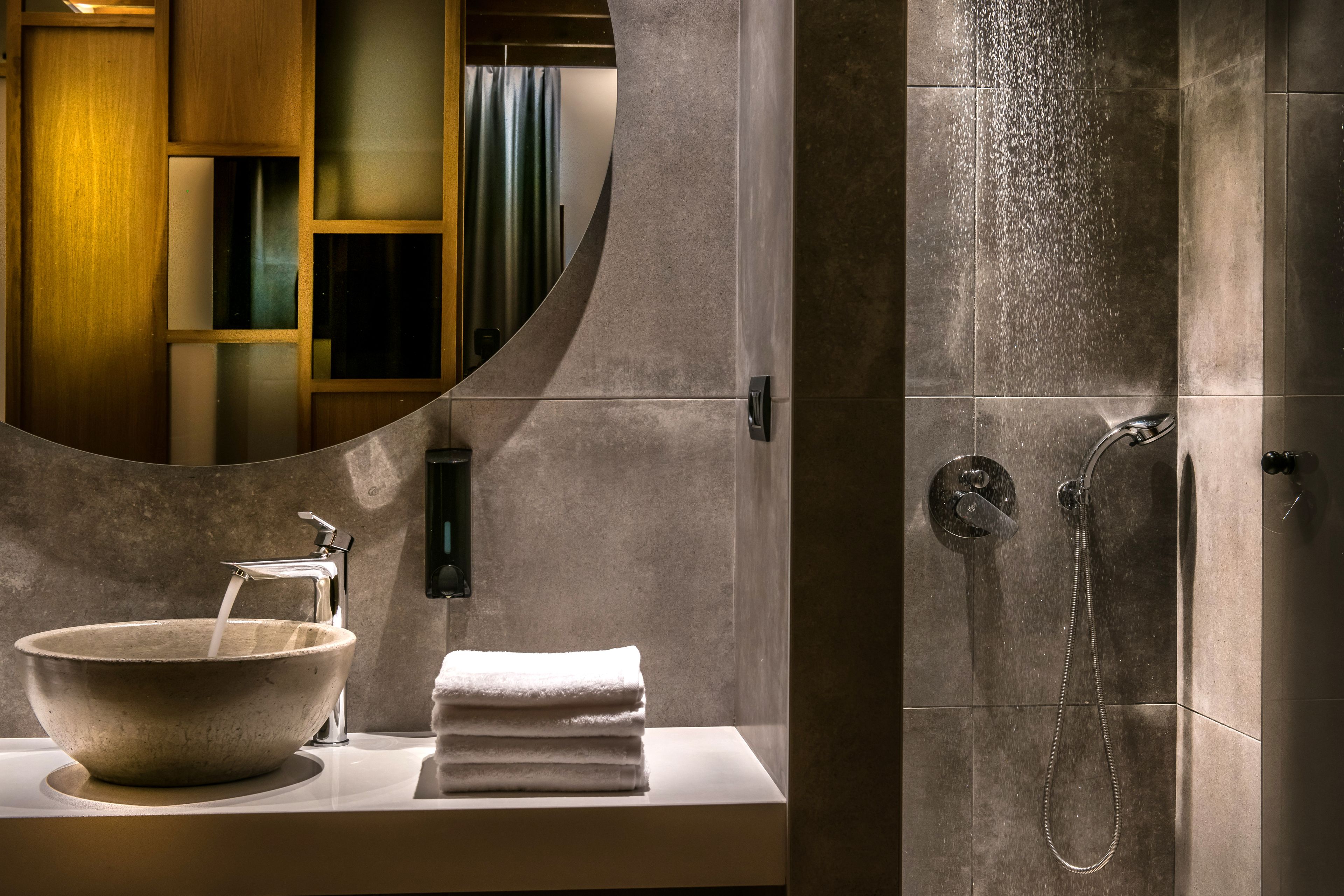 A bathroom with a large mirror, a stone sink, a towel, and a shower.