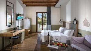 Une chambre d’hôtel avec un plafond en bois, un lit, un bureau, une chaise, un canapé et une table à manger agrémentée de fruits et de verres.
