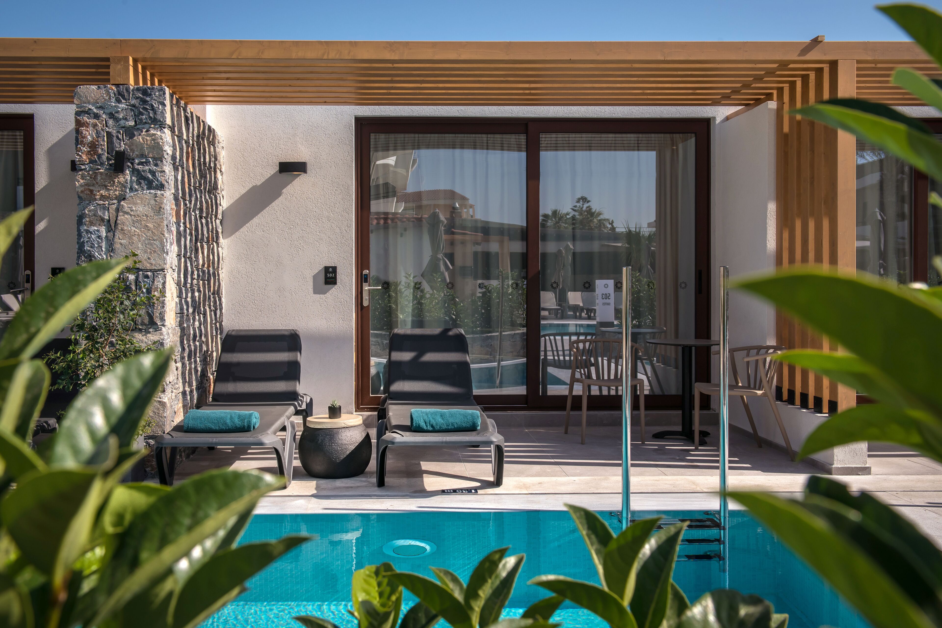 A poolside area with two lounge chairs, a table, and a stone wall.