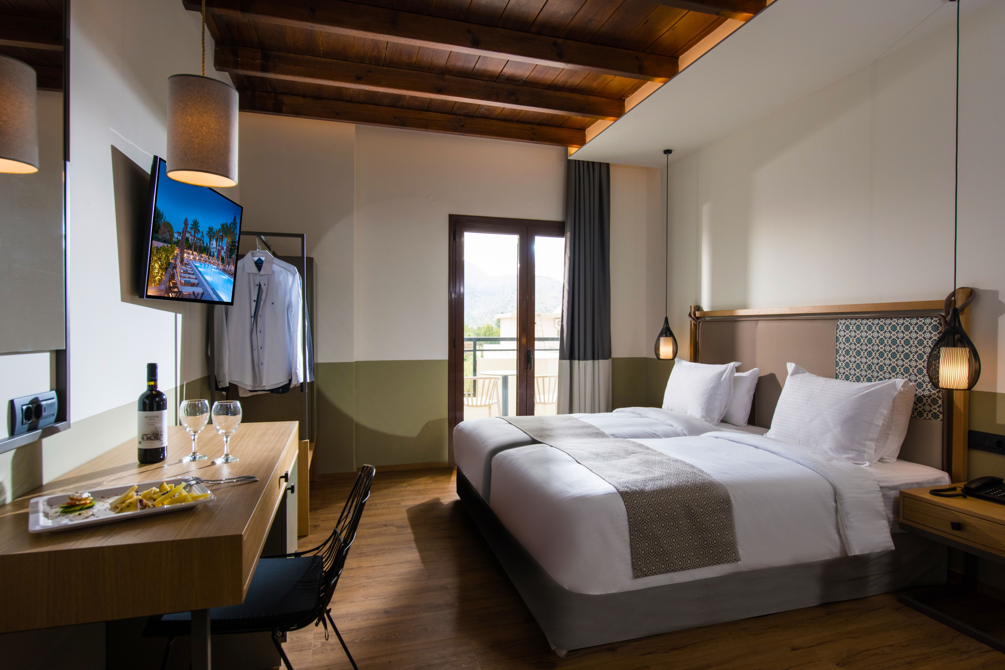 A hotel room with a bed, bedside table, TV, and a dining area with a table and chairs.