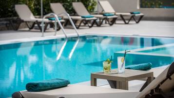 Un área junto a la piscina con sillones de descanso, una mesa con una bebida y una toalla.