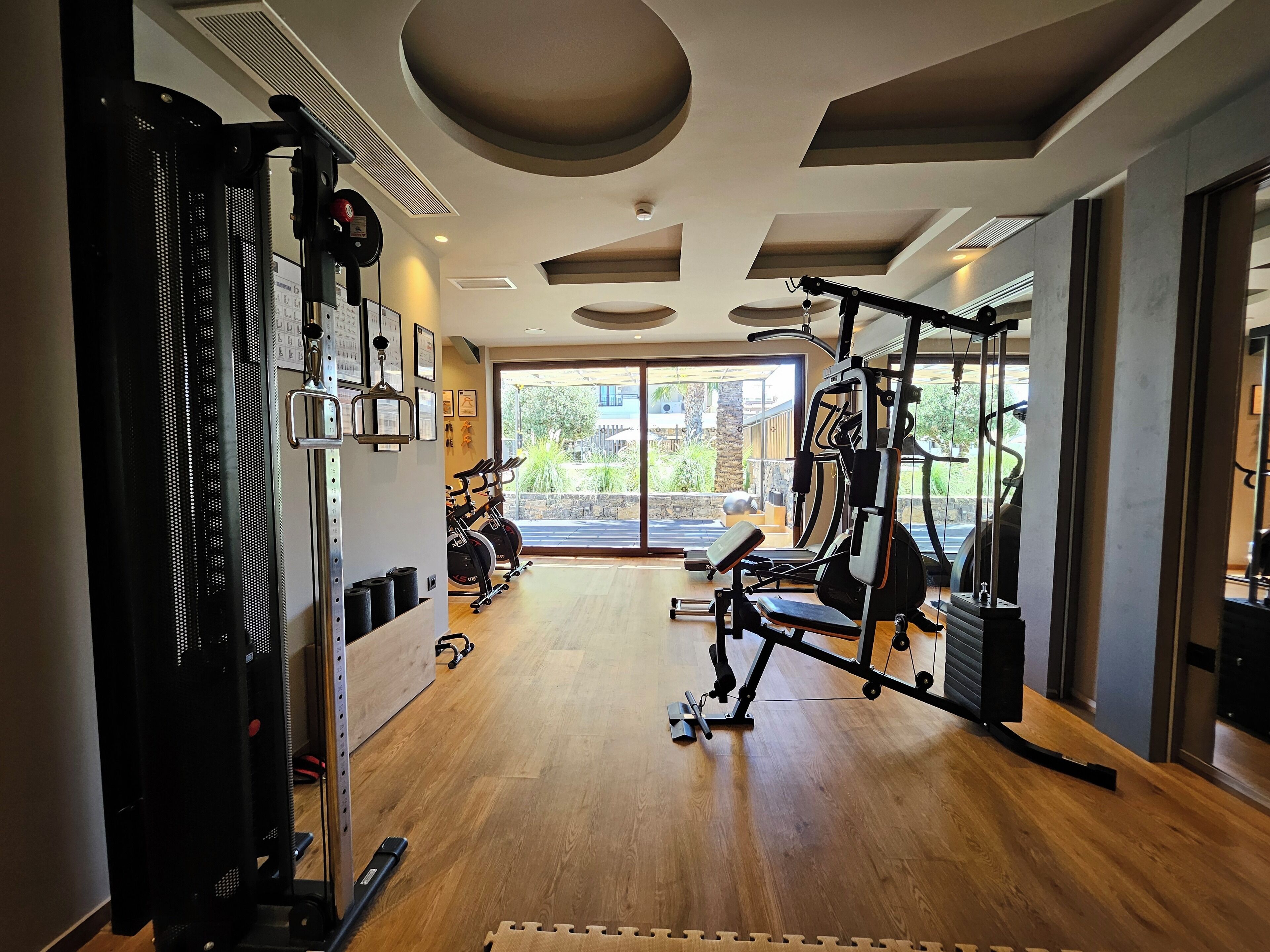 Une salle de sport équipée de matériel d’exercice, dotée d’un plancher en bois et de grandes fenêtres donnant sur l’extérieur.