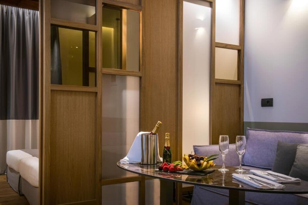 Habitación de hotel con una mesa de vidrio dispuesta con frutas, una botella de champán y copas.
