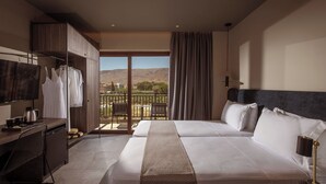 Une chambre d’hôtel avec un grand lit, un bureau, une télévision et un balcon offrant une vue sur les montagnes.