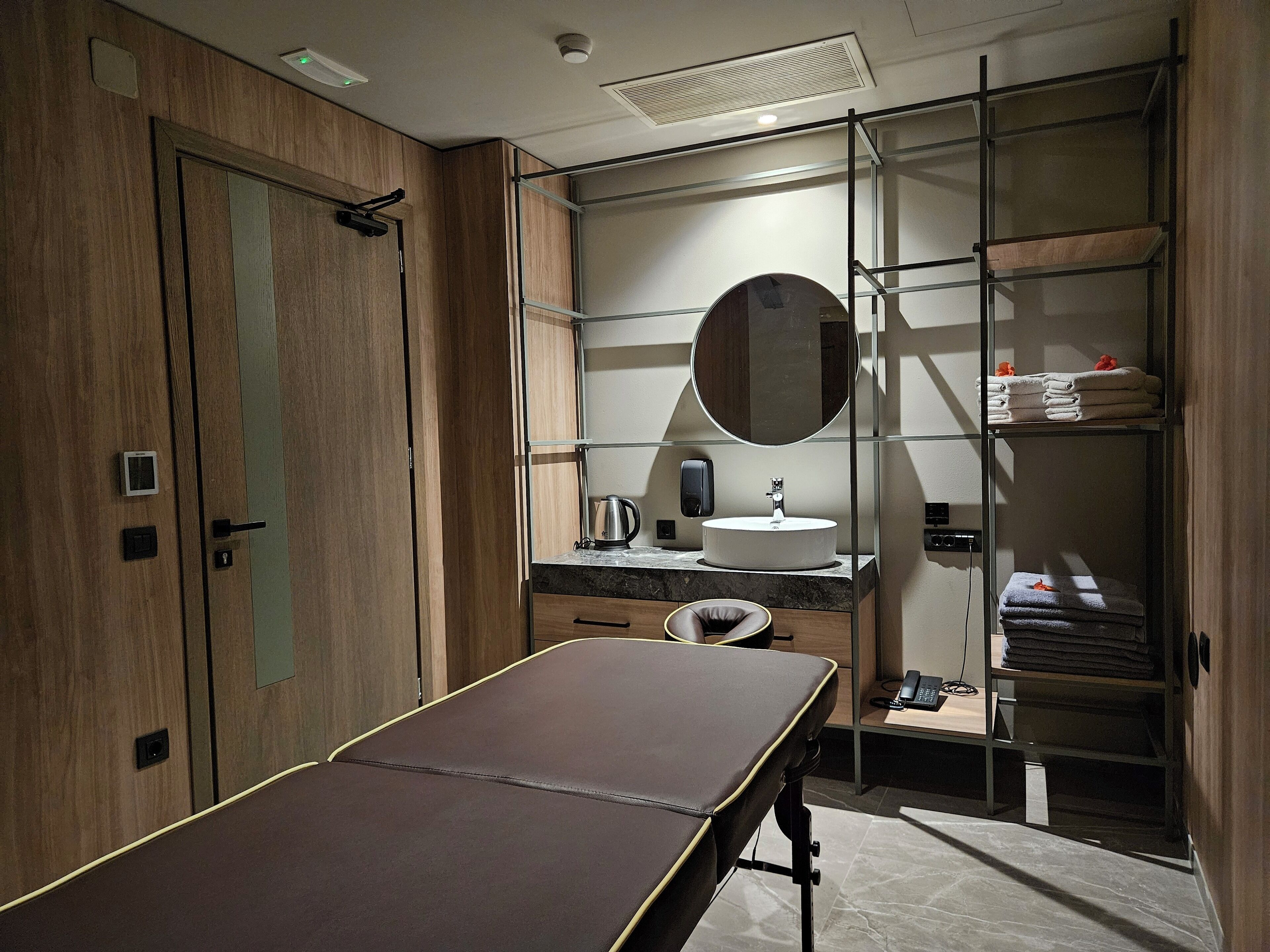 A modern bathroom with a wooden vanity, a round mirror, a sink, and a towel rack.