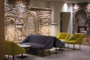 Un interior moderno con una pared de piedra, un sofá, dos sillones amarillos y una pequeña mesa.