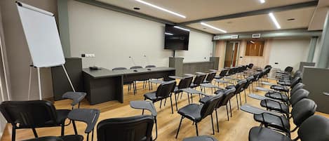 A conference room with rows of chairs, a whiteboard, and a presentation screen.