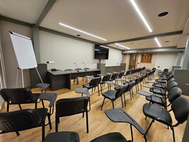 Un salón de conferencias con filas de sillas, una pizarra y una pantalla para presentaciones.