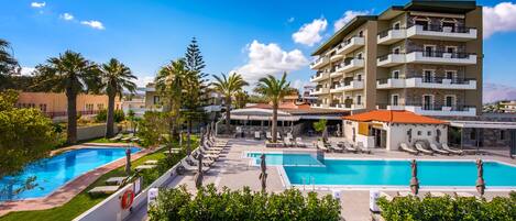 A hotel with multiple swimming pools, palm trees, and a mountainous backdrop.