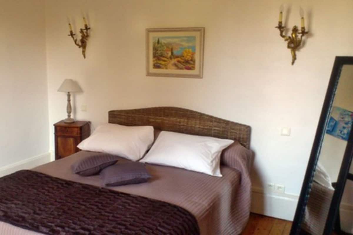 A bedroom with a bed, pillows, a lamp, and two wall-mounted light fixtures.