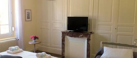 Une chambre d’hôtel avec un lit, une petite table ornée de fleurs, un téléviseur posé sur un meuble en bois et un radiateur.