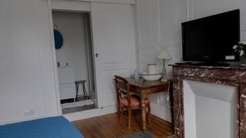 A room with a bed, a desk with a chair, a television, and a door leading to a bathroom.