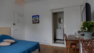 A bedroom with a bed, a desk, a chair, a potted plant, and a door leading to a bathroom.