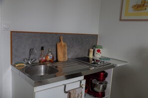 A kitchen with a double sink, a wooden cutting board, a spice jar, and a red coffee maker. - Aux Chambres du Roy (Roye)
