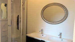 Un baño con cabina de ducha de vidrio, lavamanos doble con espejo y toallero.