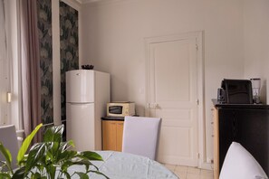 A hotel room with a bed, a desk with a computer, a refrigerator, a microwave, and a coffee maker. - Aux Chambres du Roy (Roye)