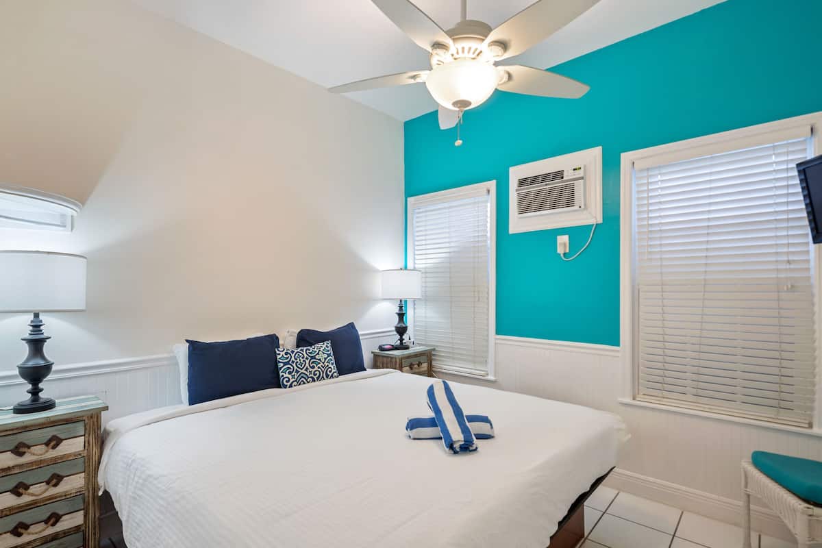 A bedroom with a large bed, a ceiling fan, and a window with blinds.