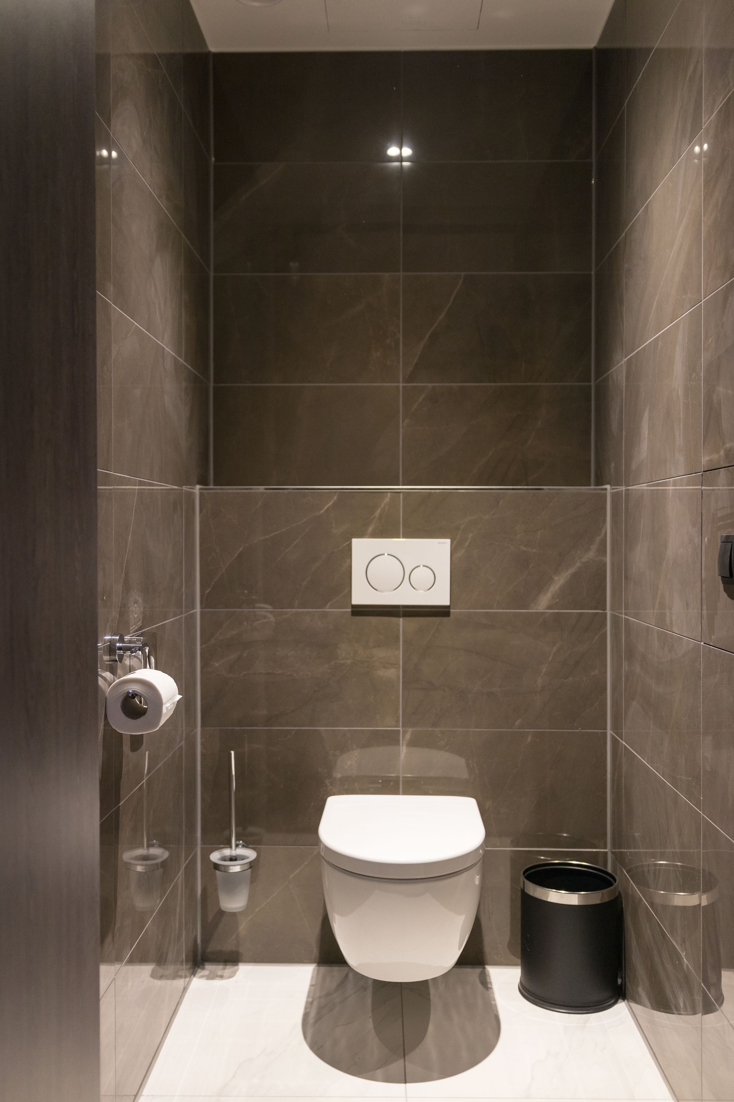 A modern bathroom with a toilet, a trash can, and a toilet paper holder.