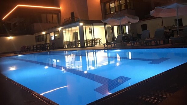 Une piscine à l’eau d’un bleu limpide, entourée de chaises longues et de parasols, et un bâtiment au design moderne et à l’éclairage chaleureux.