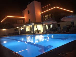 A swimming pool with a clear blue water surface, surrounded by lounge chairs and umbrellas, and a building with a modern design and warm lighting. - Oyster Boutique Hotel (Manavgat)