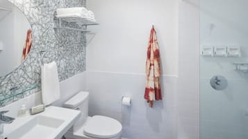 Een moderne badkamer met een douchecabine van glas, een wit toilet, een wastafel met zeepdispenser en een handdoekrek met een handdoek.